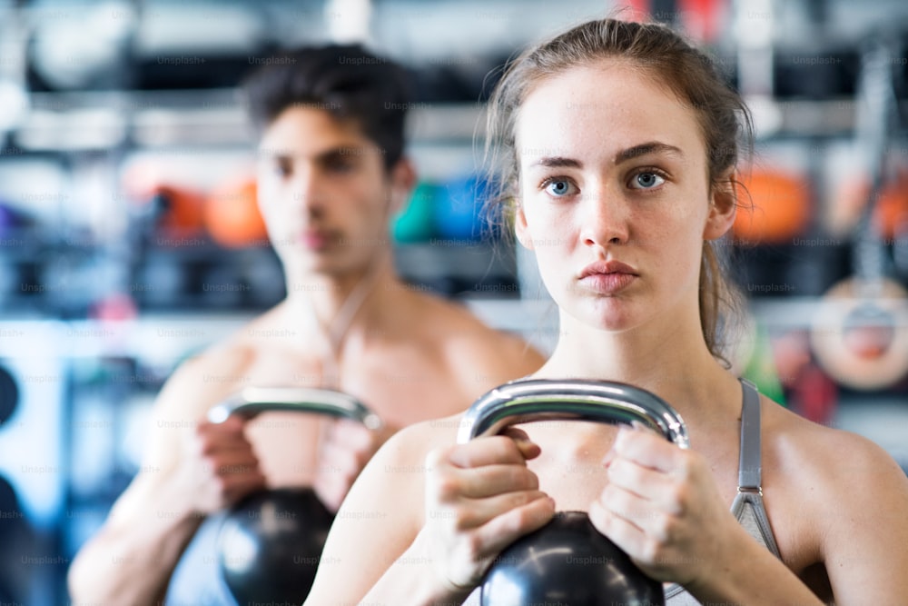 Hermosa pareja joven en forma haciendo entrenamiento de fuerza, haciendo ejercicio con pesas rusas en el gimnasio moderno.