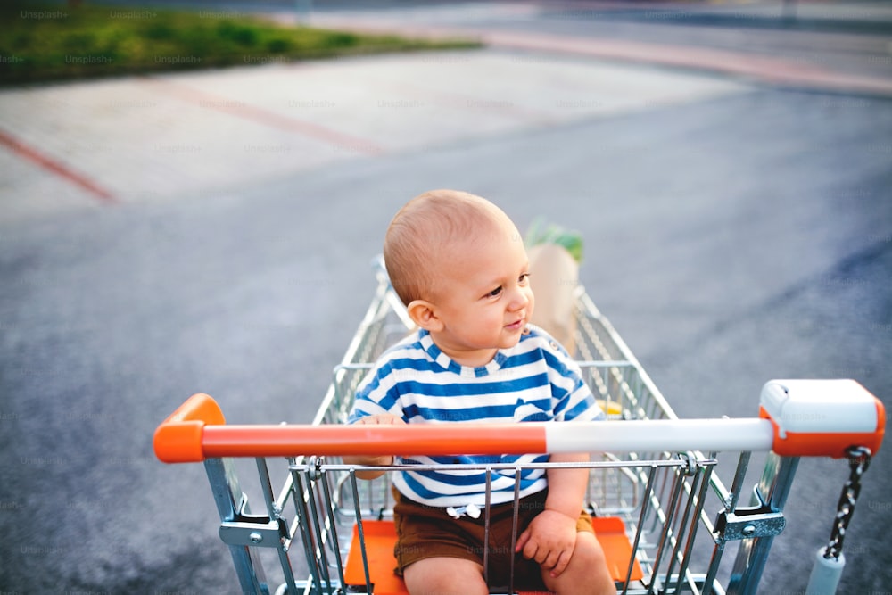 Baby boy sitting in the shopping trolley outside in the car park.
