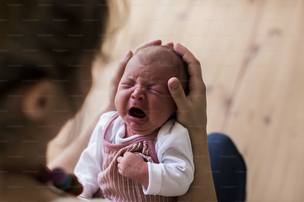 Giovane madre irriconoscibile a casa che tiene in braccio la sua neonata che piange.