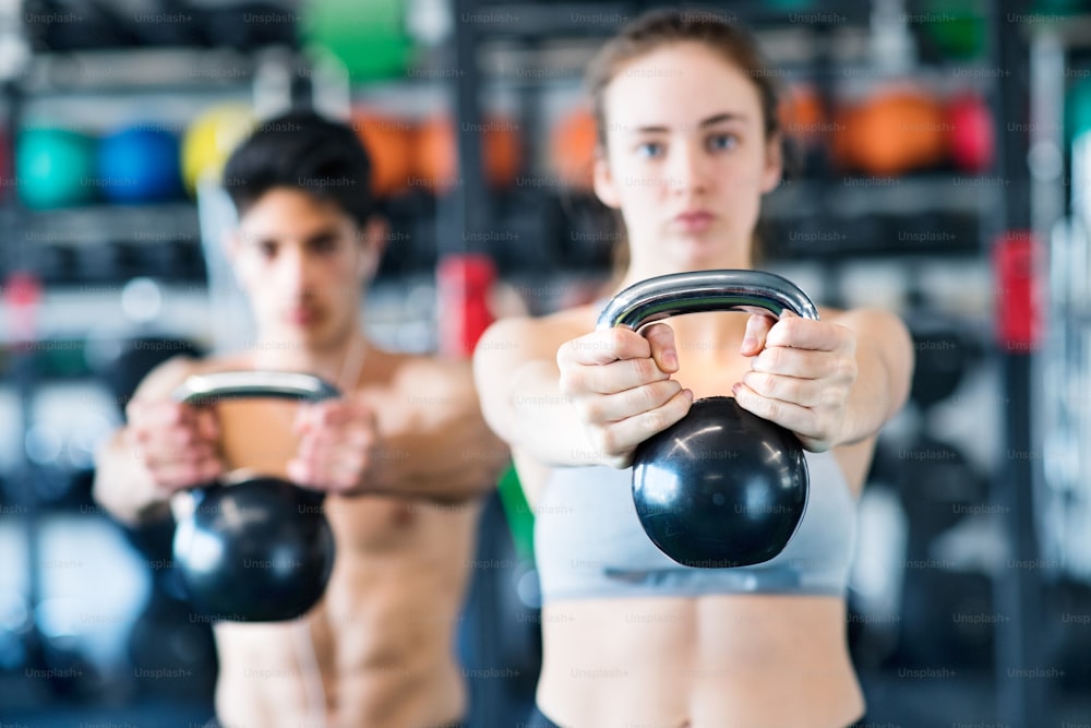 Beautiful young fit couple doing strength training, exercising with kettlebell in modern gym.
