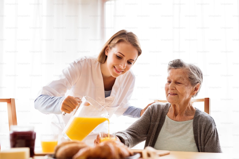 訪問中の健康訪問者と高齢の女性。オレンジジュースを注ぐ看護師と年配の女性。