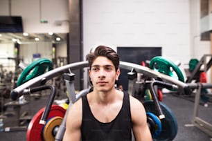 Young fit hispanic man in gym going to work out on fitness machine, flex muscles. Bodybuilder prepared for training, going to do shoulder press.