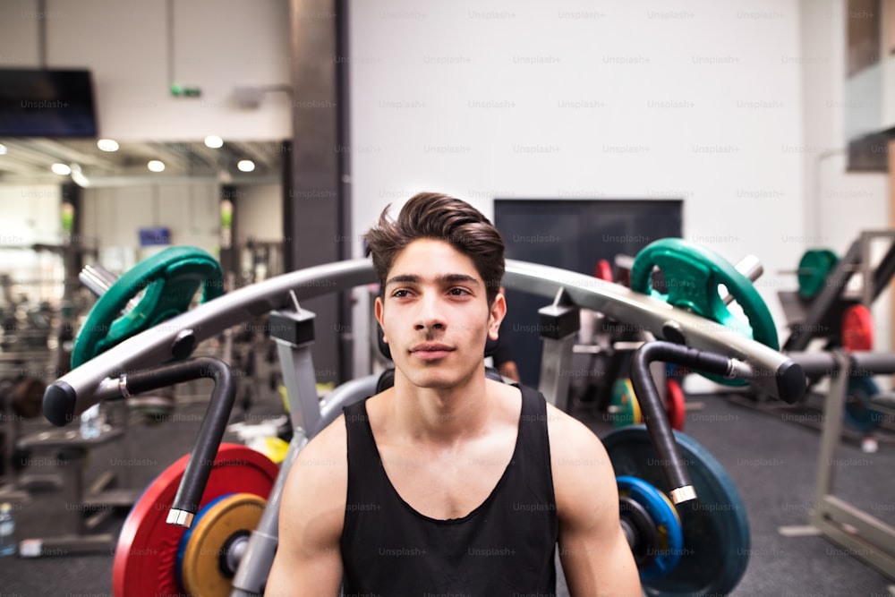 Foto Joven hombre hispano en forma en el gimnasio que va a hacer ejercicio  en la máquina de fitness, flexiona los músculos. Culturista preparado para  entrenar, va a hacer press de hombros. –