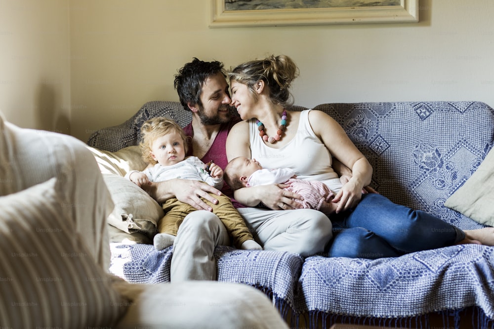 Beautiful young parents at home sitting on couch with their cute son and baby daughter.