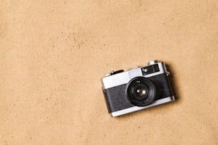 Vintage camera laid on beach. Summer vacation composition. Sand background, studio shot, flat lay. Copy space.