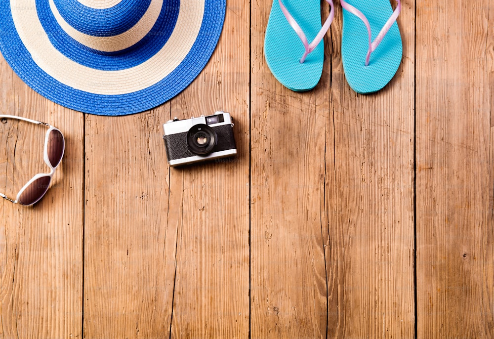夏休みの構図。木製の背景にサングラス、帽子、黄色のビーチサンダル、ビンテージカメラ。スタジオショット、フラットレイ。スペースをコピーします。