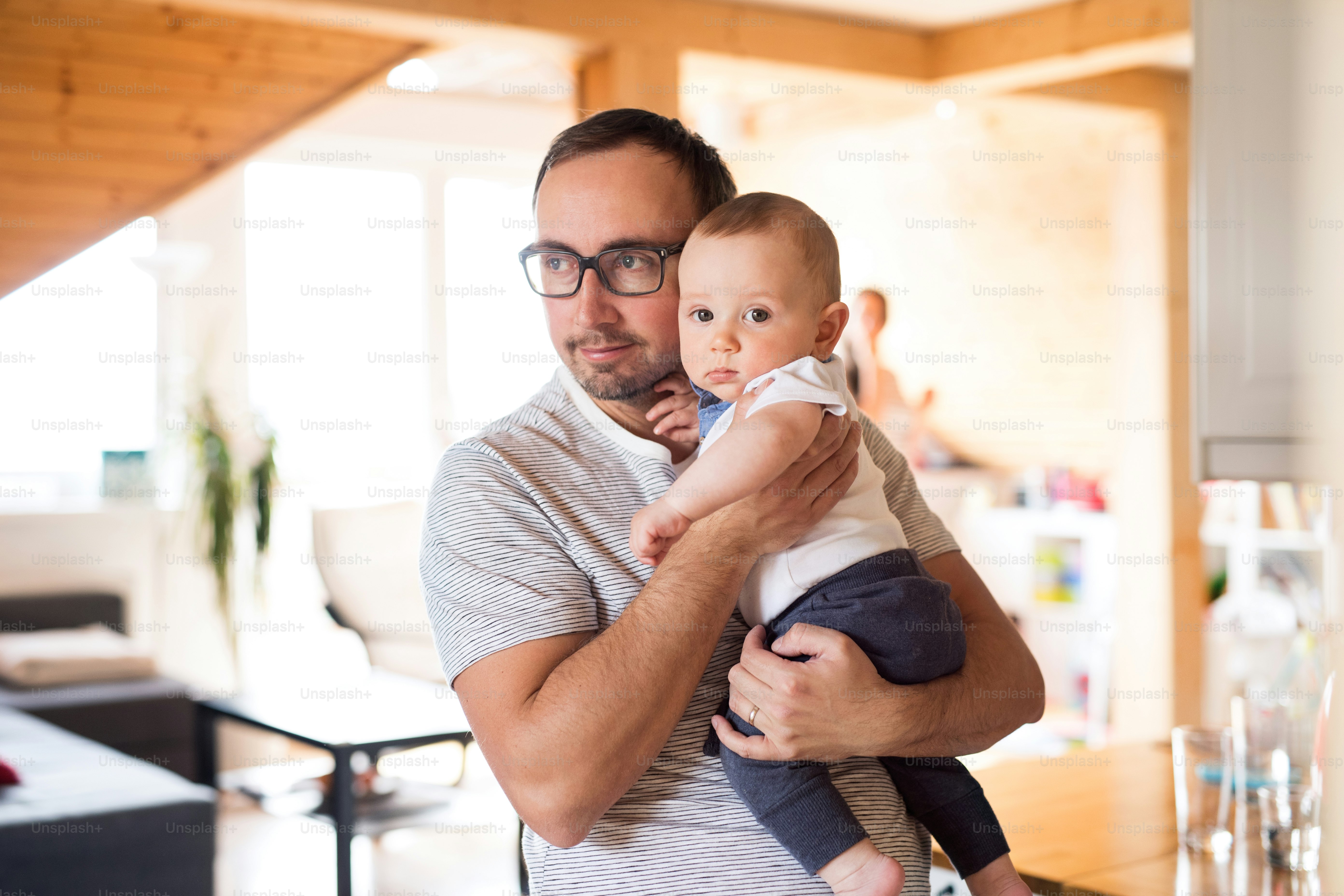 Ayah muda di rumah menggendong bayi laki-lakinya yang lucu di pelukannya