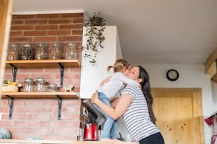 Schöne junge Mutter zu Hause umarmt ihre süße kleine Tochter, die auf der Küchenarbeitsplatte steht.