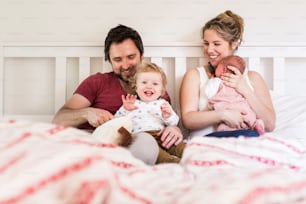 Beautiful young parents at home sitting in bed with their cute son and baby daughter.