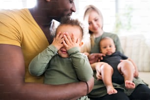 Linda família inter-racial jovem em casa com sua filha fofa e filho bebê.