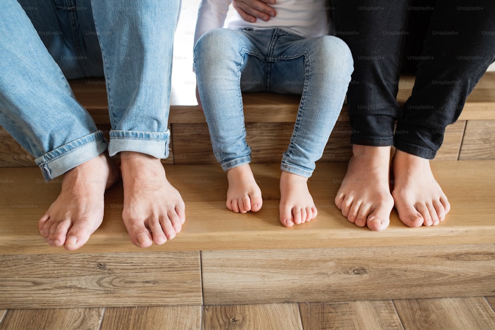 Beautiful young family sitting on stairs. Close up of bare feet of mother, father and daughter.