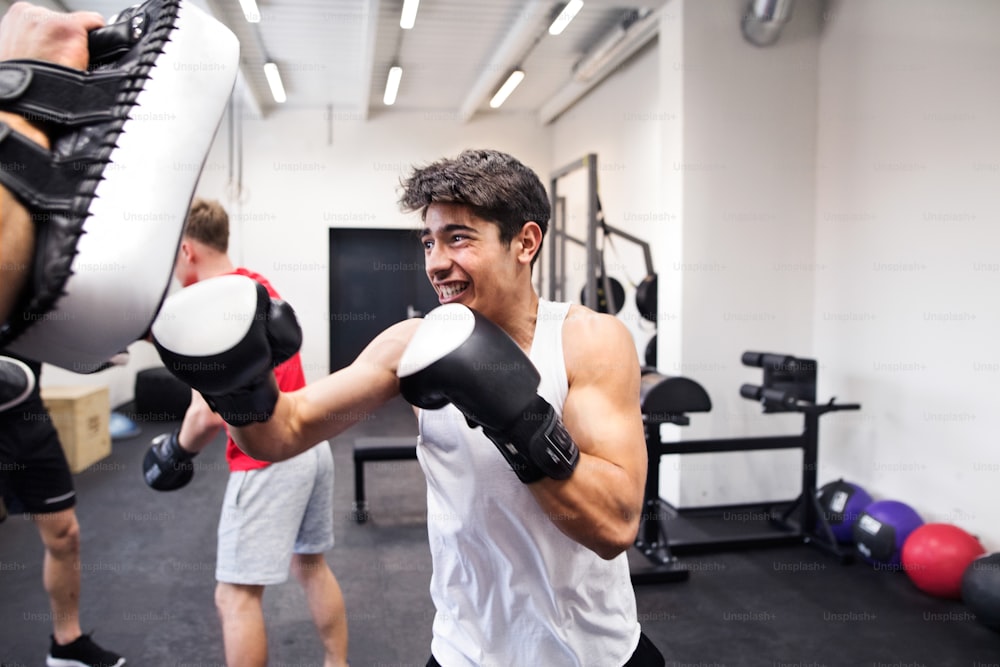Handsome fit hispanic man in gym boxing with his unrecognizable personal trainer