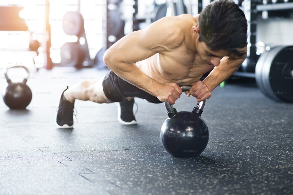 Fit hispanic man doing strength training, doing push ups on kettlebell in modern gym.