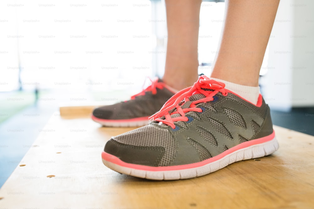 Close up of feet of young woman in gym standing on wooden box. Sport shoes.