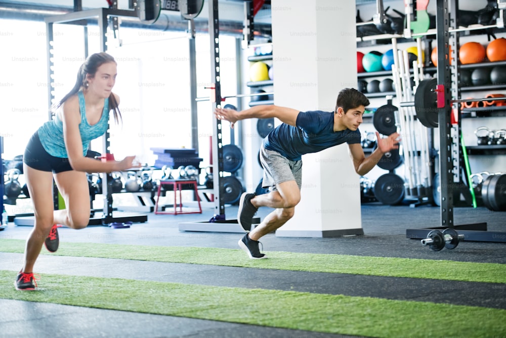 Young fit couple in gym fast running. Young man and woman doing intense training session. Sports training in the gym.