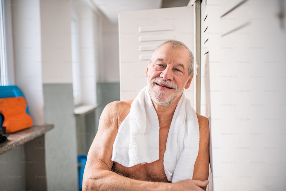 Älterer Mann steht an den Schließfächern in einem Hallenbad. Aktiver Rentner mit Spaß am Sport.