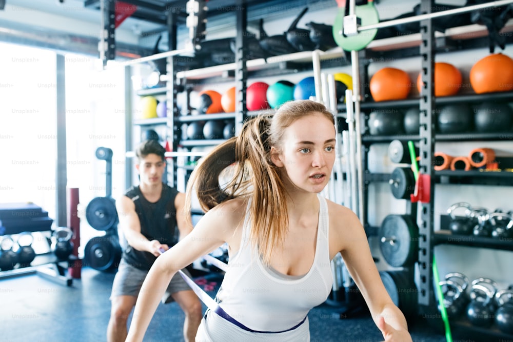 Strong woman using a resistance band in her exercise routine. Young fit couple performs fitness exercise in modern gym gym.