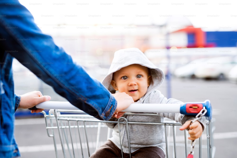 Unrecognizable mother with baby boy in the car park, going shopping. Toddler boy sitting in a shopping trolley.