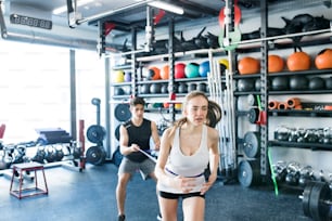 Strong woman using a resistance band in her exercise routine. Young fit couple performs fitness exercise in modern gym gym.