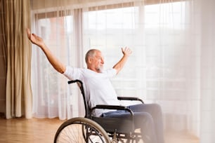 Senior man sitting on wheelchair at home, arms stretched.