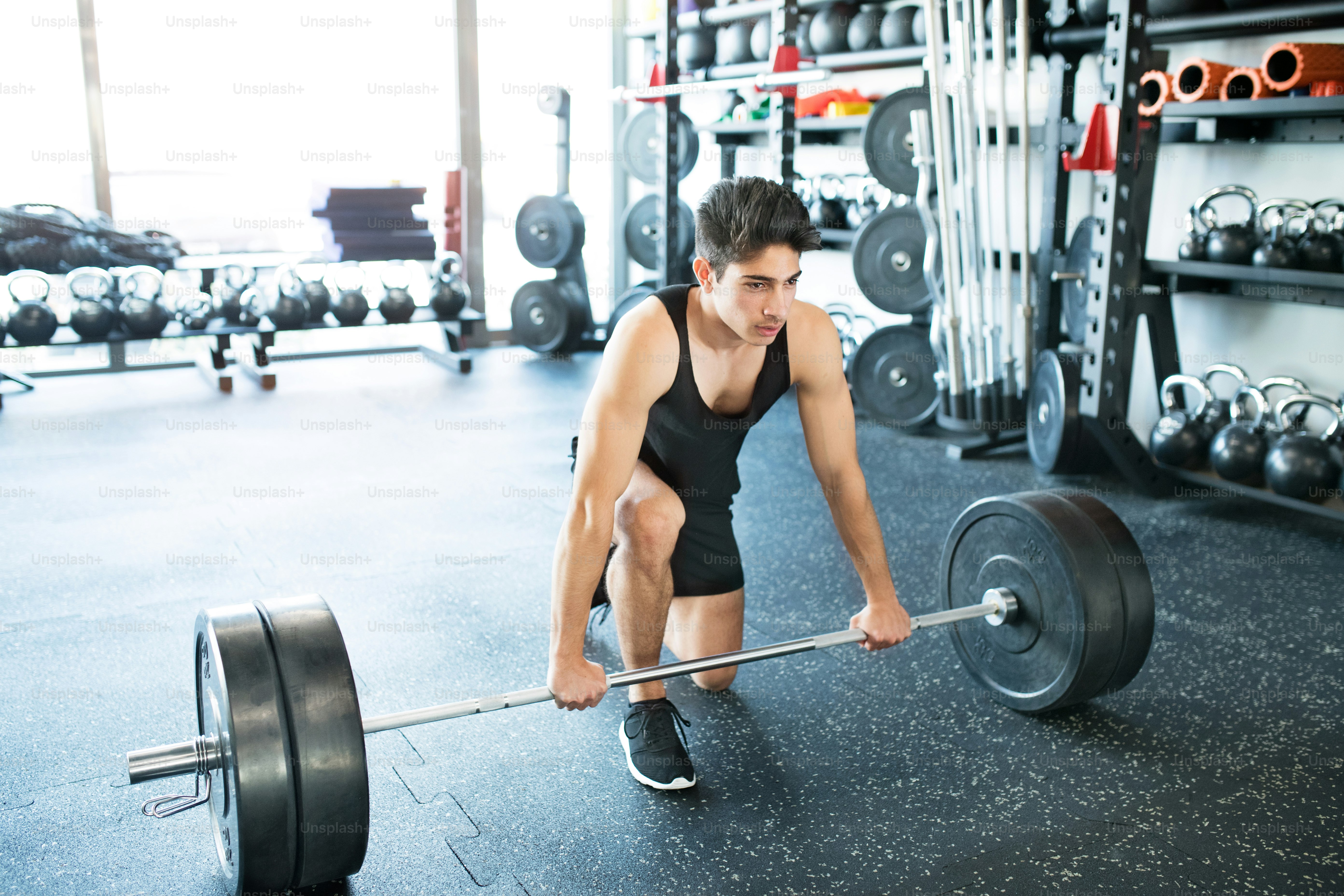 Joven hombre hispano en forma en el gimnasio levantando pesas pesadas, flexionando los músculos
