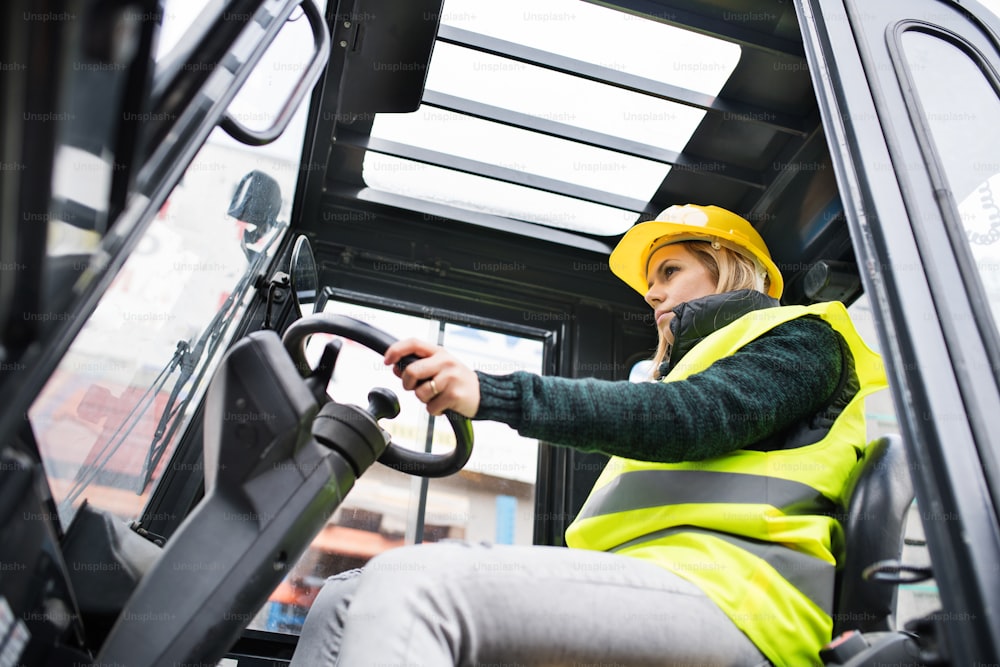Female forklift truck driver in an industrial area. A woman sitting in the fork lift outside a warehouse.