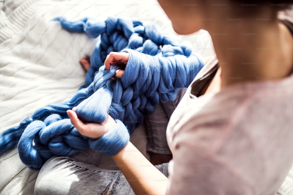 젊은 여성의 중소기업. 알아볼 수 없는 여자가 모직 담요를 손으로 뜨개질하고 있다.