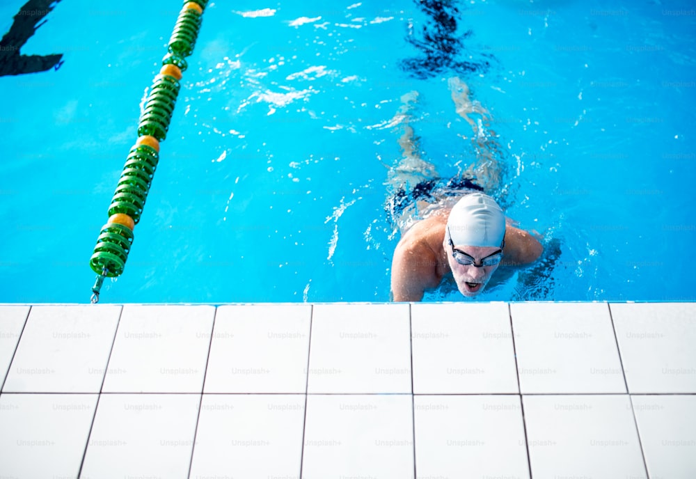 Homme âgé nageant dans une piscine intérieure. Retraité actif qui fait du sport.