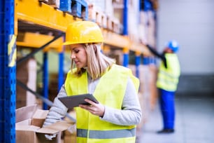 Young woman worker or supervisor with tablet. Warehouse workers controlling stock.
