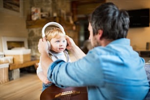 Unrecognizable young father at home with guitar, his little son wearing earphones and listening music.