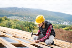 Female worker on the building site. Young woman working as a roofer. House construction.