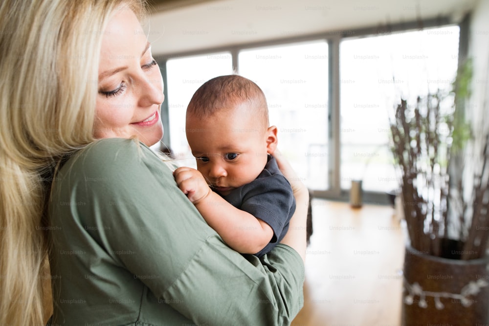 Beautiful young blonde mother at home holding her little mixed-race baby son in the arms.