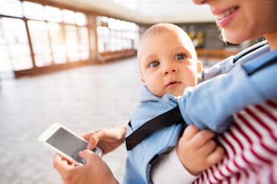 Giovane madre irriconoscibile con smartphone e bambino in viaggio. Una bella donna e suo figlio all'interno dell'edificio della stazione.