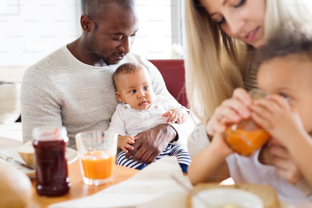 Schöne junge interrassische Familie zu Hause mit ihrer süßen Tochter und ihrem kleinen kleinen Sohn, die zusammen frühstücken.
