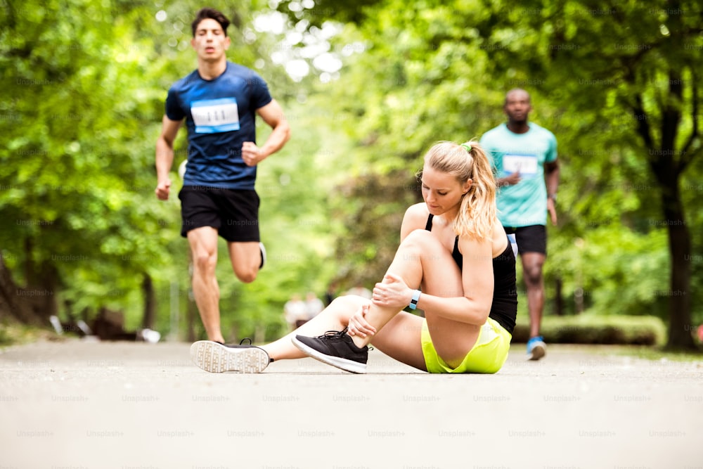 Junge Frau beim Wettkampf sitzt mit verstauchtem Knöchel auf dem Boden. Läufer mit Verletzung.