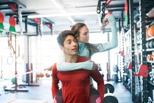 Young fit couple in modern gym gym. Man carrying woman on his shoulders.
