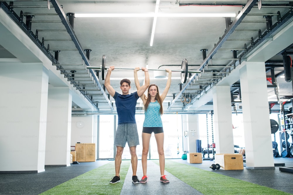 Beautiful young fit couple exercising in modern gym, lifting heavy barbell.