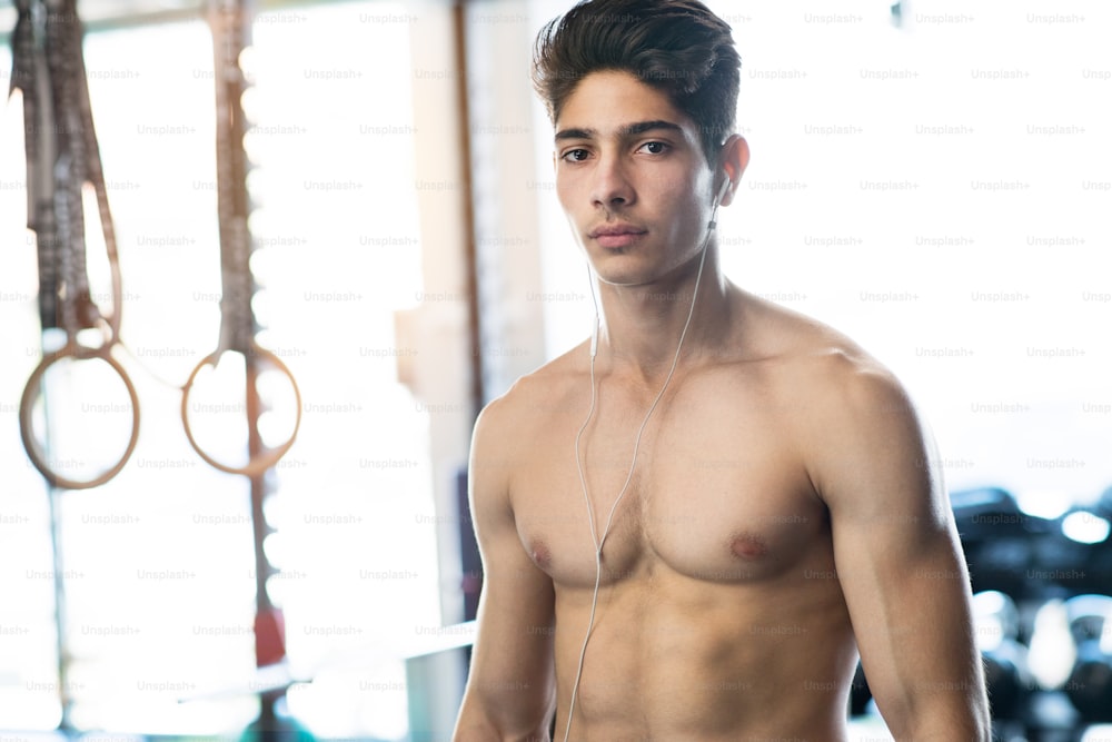 Young fit hispanic man with bare chest in modern gym doing strength training.