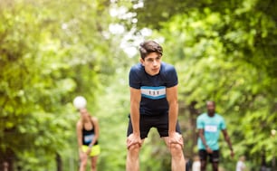 Jeune homme hispanique en forme avec des amis dans le parc se reposant après avoir terminé la course.