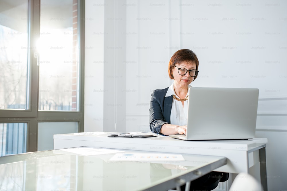 Elegante Geschäftsfrau im Anzug arbeitet mit Laptop im weißen Büro