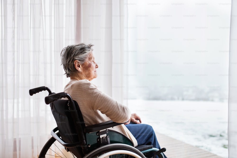 Mujer mayor en silla de ruedas en casa mirando por la ventana.