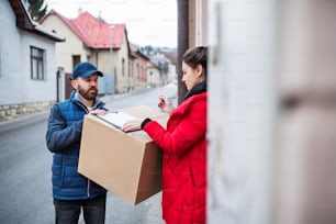 Young woman receiving parcel from delivery man at the door - courier service concept.