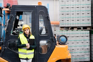 Woman forklift truck driver in an industrial area. A woman standing in front of the fork lift truck outside a warehouse.