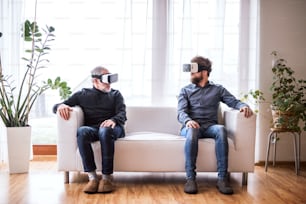 Hipster son and his senior father with VR goggles at home. Two generations indoors, having fun.