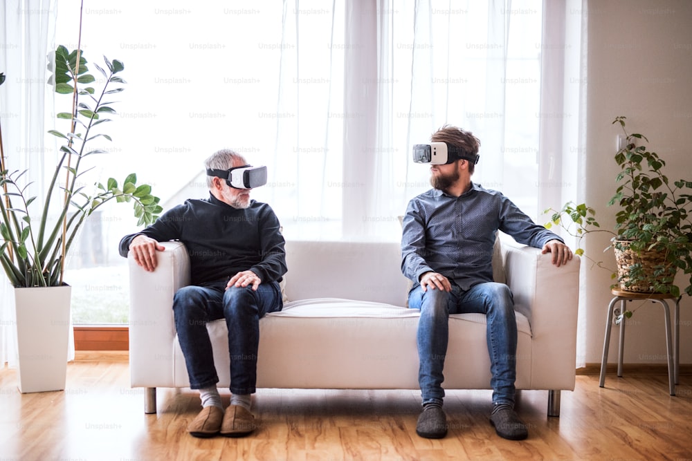 Hipster son and his senior father with VR goggles at home. Two generations indoors, having fun.