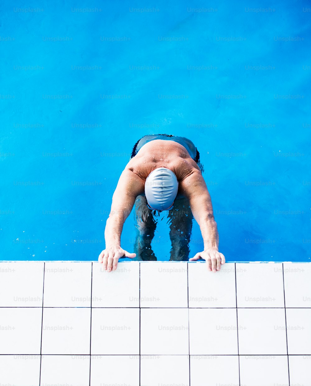 Homem sênior em pé na água em uma piscina coberta. Pensionista ativo desfrutando de esporte. Vista superior.
