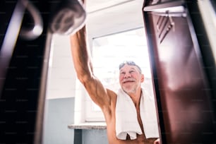 Senior man standing by the lockers in an indoor swimming pool. Active pensioner enjoying sport.