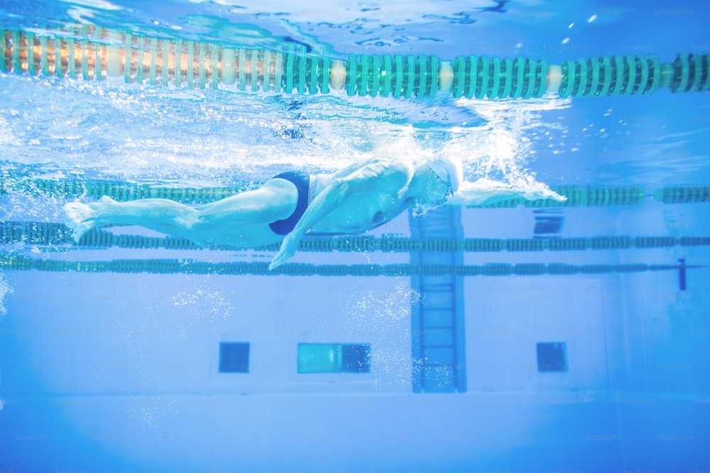 Älterer Mann schwimmt unter Wasser in einem Hallenbad. Aktiver Rentner mit Spaß am Sport.