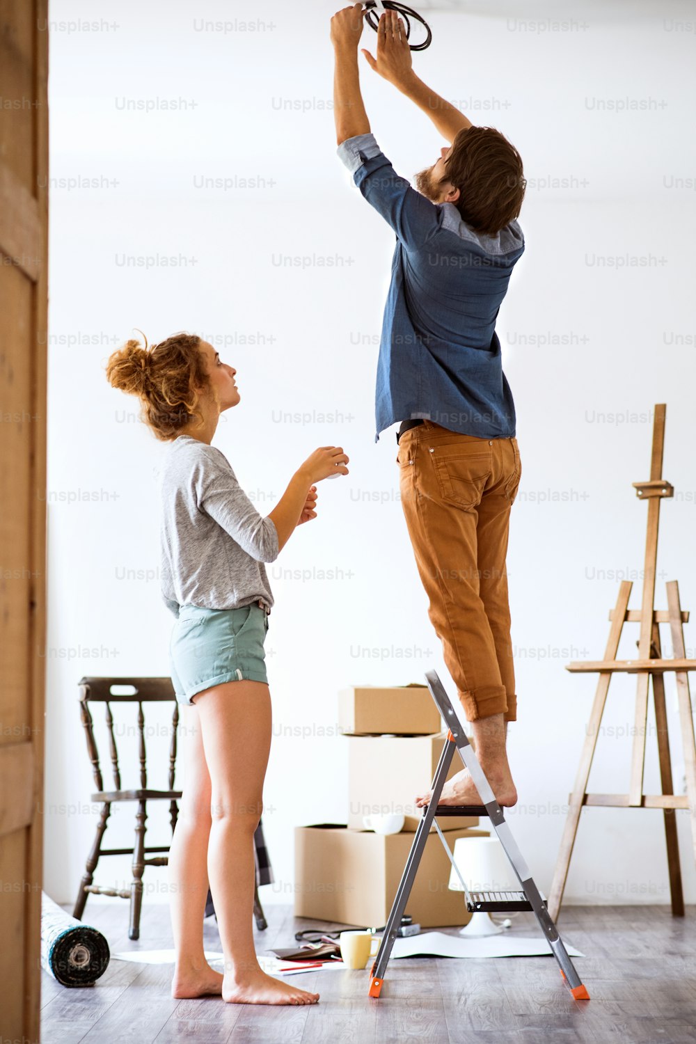Young married couple moving in new house, changing a light bulb.