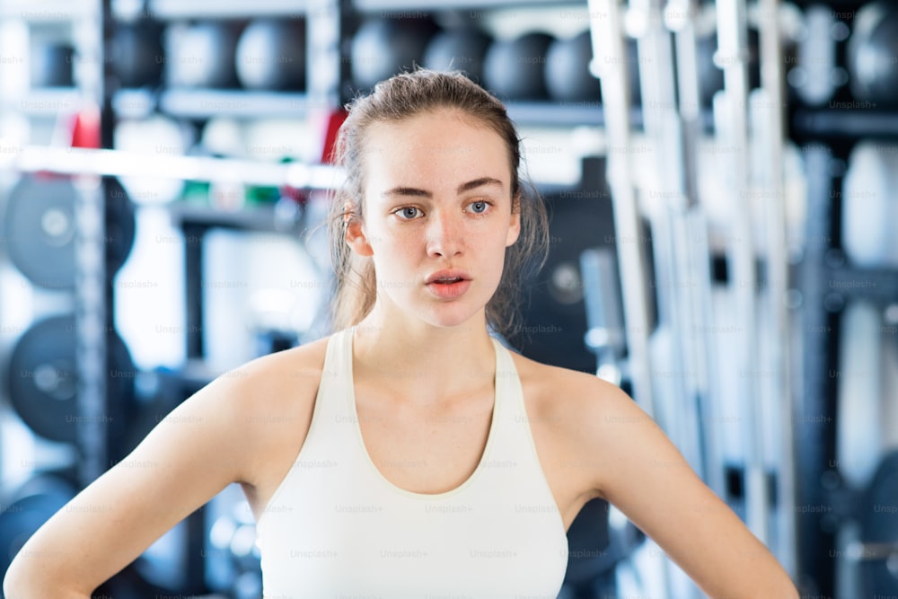 Face of beautiful young fit woman in gym in white tank top, resting